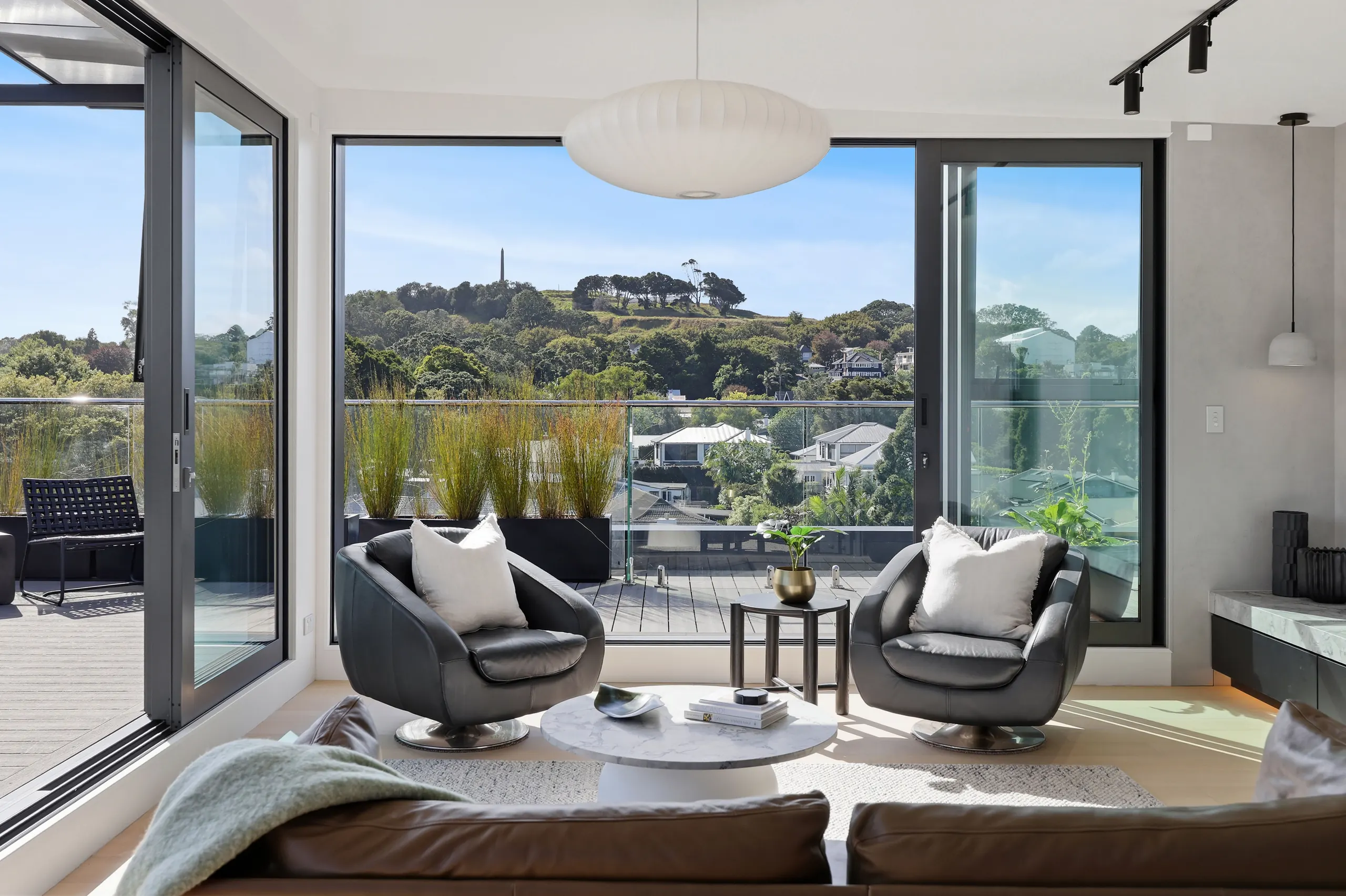 Inside the Logan penthouse, Epsom — living room opening to the terrace, One Tree Hill beyond
